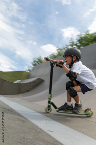 Obraz na płótnie A cute little boy rides a scooter in a skatepark. w salonie