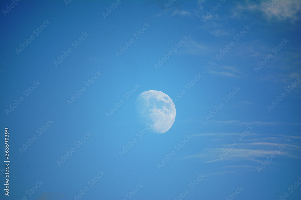 Moon in the daytime, blue sky with small clouds