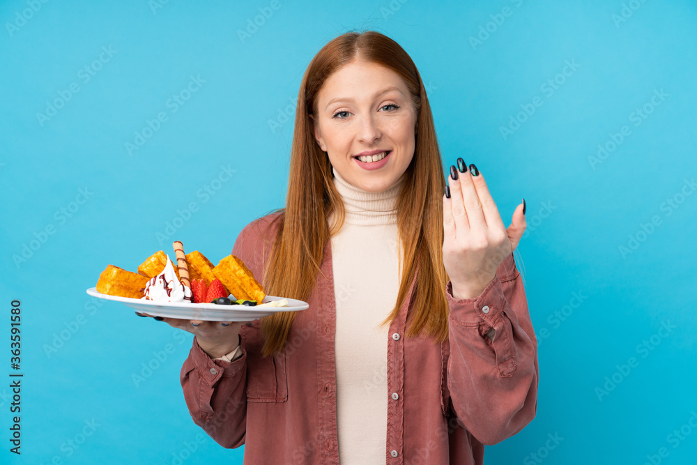 Young redhead woman holding waffles over isolated background inviting to come with hand. Happy that you came Young redhead woman holding waffles over isolated background inviting to come with hand. Happy that you came