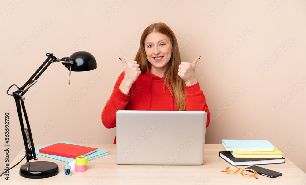 Young student woman in a workplace with a laptop with thumbs up gesture and smiling Young student woman in a workplace with a laptop with thumbs up gesture and smiling