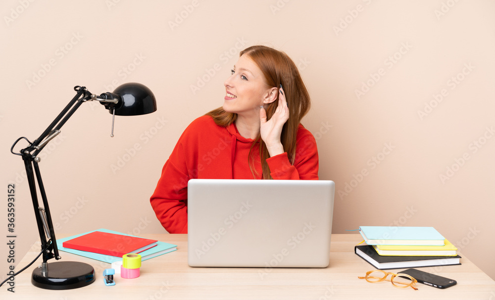 Young student woman in a workplace with a laptop listening to something by putting hand on the ear Young student woman in a workplace with a laptop listening to something by putting hand on the ear