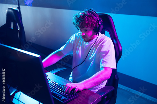 Cyber sport. Fully concentrated professional cybersport gamer playing important match. Caucasian male model practicing, training before tournament alone in neon light. E-sport, gamer, streamer. © master1305