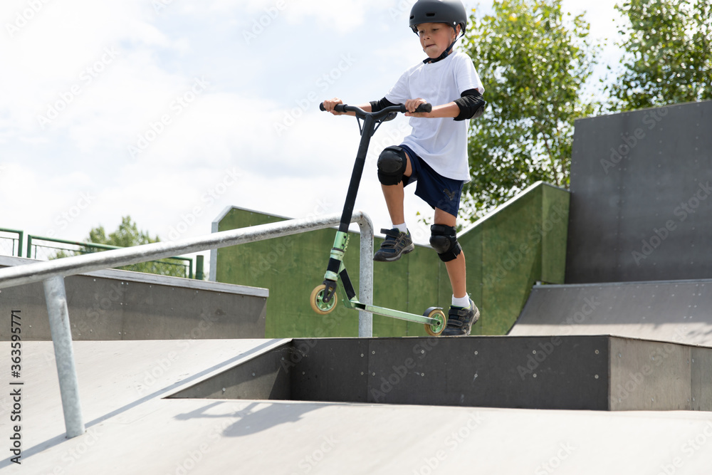 A cute little boy rides a scooter in a skatepark.