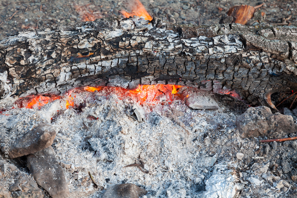 Close-up of embers from gray ash with streaks of orange flame in a bonfire in nature during the preparation of barbecue on the weekend. Pattern for wallpaper or for design. Close-up of embers from gray ash with streaks of orange flame in a bonfire in nature during the preparation of barbecue on the weekend. Pattern for wallpaper or for design.