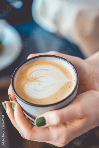 Woman holding a almond milk cappuccino, with latte art of a heart in the foam. Vintage coffee barista concept. 