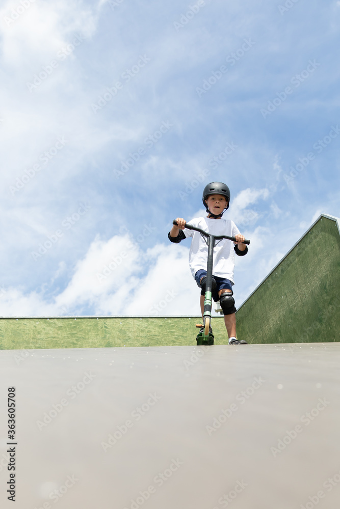 A cute little boy rides a scooter in a skatepark.