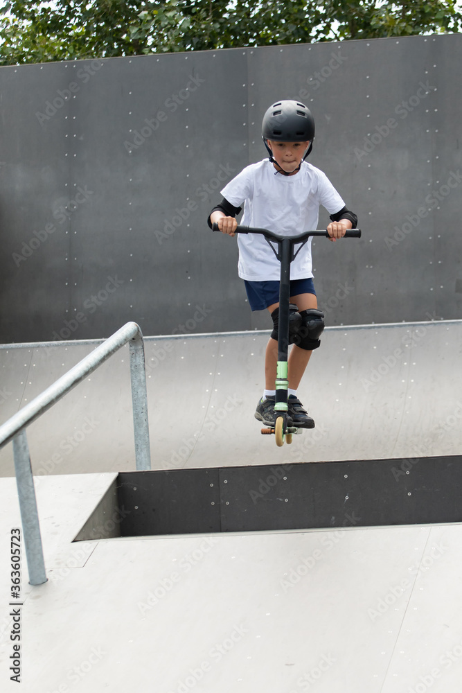 A cute little boy rides a scooter in a skatepark.