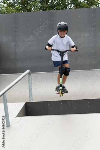 Obraz na płótnie A cute little boy rides a scooter in a skatepark. w salonie