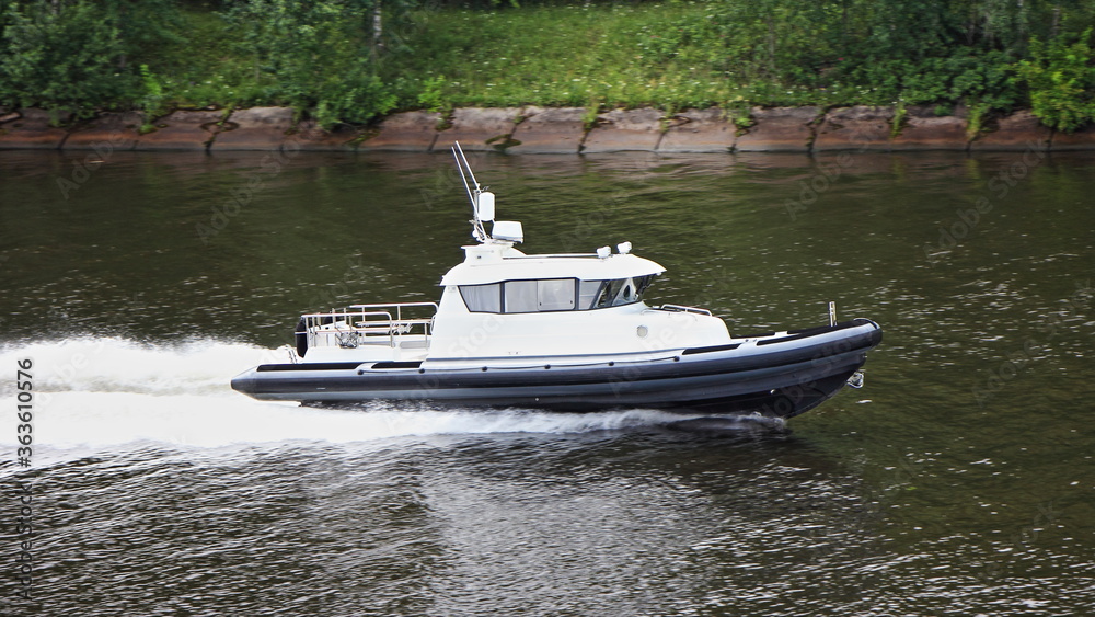Large white cabin RIB with black tubes and powerful inboard motor fast floating on water in river canal on summer day on stone shore background Large white cabin RIB with black tubes and powerful inboard motor fast floating on water in river canal on summer day on stone shore background