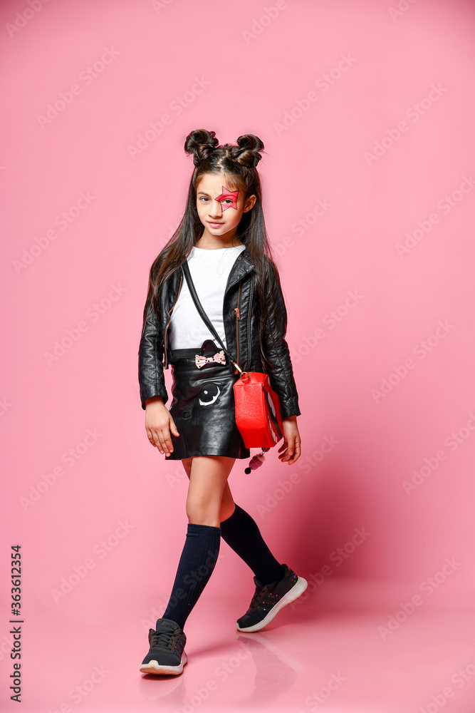 Little fashionable girl hipster punk - dressed in a leather jacket and skirt, black loaches and a white T-shirt, with a funny hairstyle and painted makeup star on her face. Little fashionable girl hipster punk - dressed in a leather jacket and skirt, black loaches and a white T-shirt, with a funny hairstyle and painted makeup star on her face.