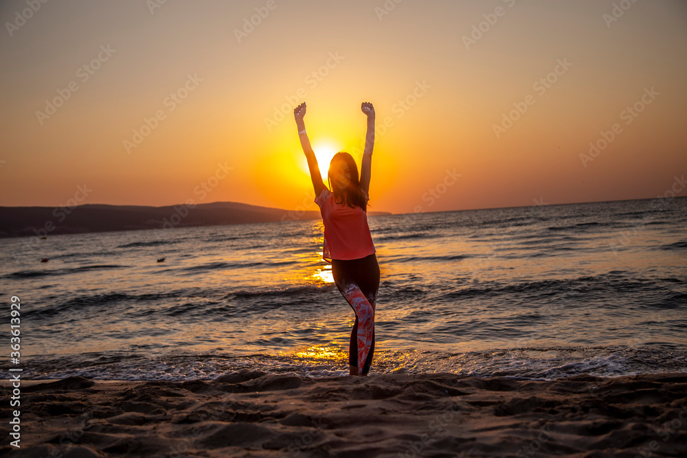 The happy woman smiles and standing with arms up at the beach during beautiful sunrise. Freedom and relax concept