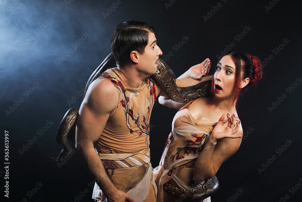 Fototapeta premium Beautiful man and woman Adam and Eve, posing with nature snake on a black background