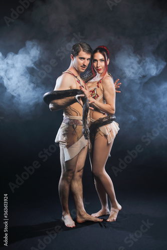 Beautiful man and woman Adam and Eve, posing with nature snake on a black background