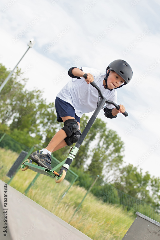 The boy jumps on a scooter.