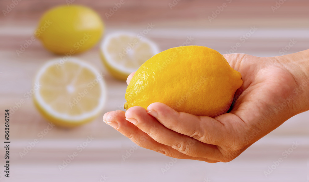 Fresh lemon in a woman's hand and a slice of lemon on a wooden table. Fresh lemon in a woman's hand and a slice of lemon on a wooden table.