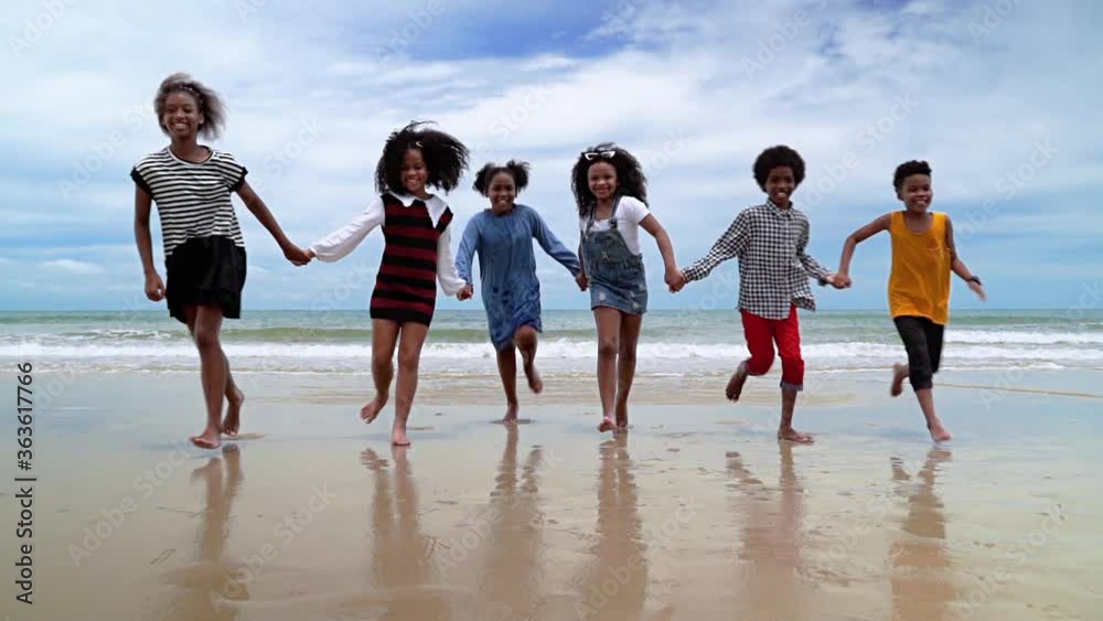 slow motion, african-American children are holding hands running on the beach in the summer
