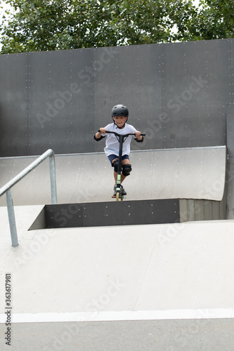 Obraz na płótnie A cute little boy rides a scooter in a skatepark. w salonie