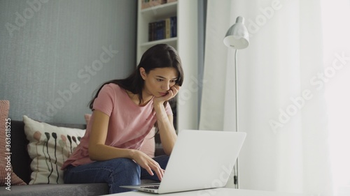 Boring woman working with laptop comfortable sitting at home