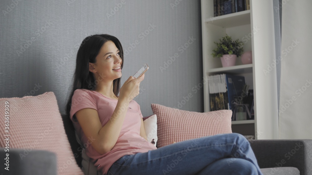Happy girl using voice recognition on phone to record a message sitting on a couch in the night at home Happy girl using voice recognition on phone to record a message sitting on a couch in the night at home