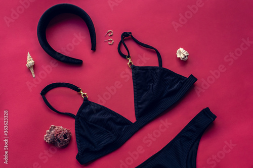 Top view of black bikini swimsuit swimwear with beach accessories over pink background. Summer vacation concept. Flat lay