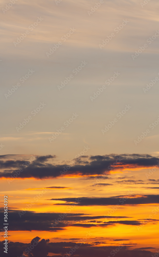 Sunset sky, lines of dark clouds, orange haze. Vertical beautiful natural background.