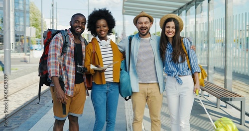 Fotografia Portrait of multiethnic males and females tourists standing together in hugs at bus stop on summer day