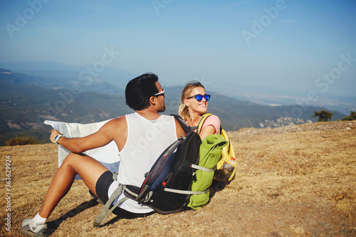 Two cheerful best friends looking back on the mountain which they overcame during walking tour in sunny day, young man and woman wanderers enjoying beautiful landscape during summer hike overseas