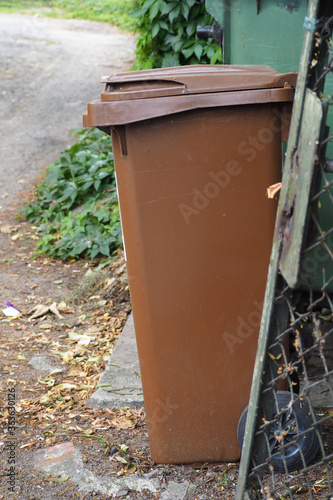 a brown plastic trash can stands on the street near the fence. biowaste tank during garbage sorting © NataSel