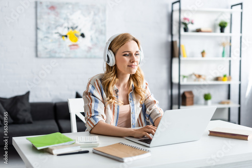 Selective focus of pretty woman working with laptop and headphones
