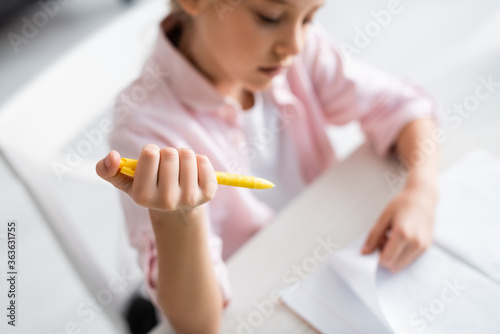High angle view of kid holding pen and looking at notebook on table