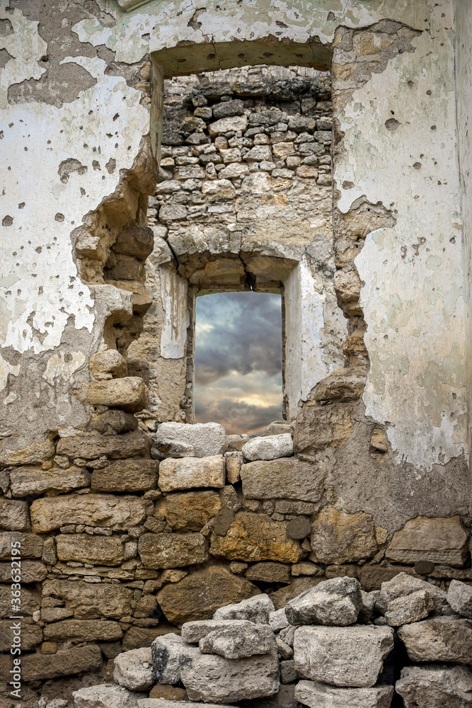 Dilapidated stone walls of medieval desolate building. Masonry, rooms with arched vaults. Stormy sky is visible through window. Selective focus.