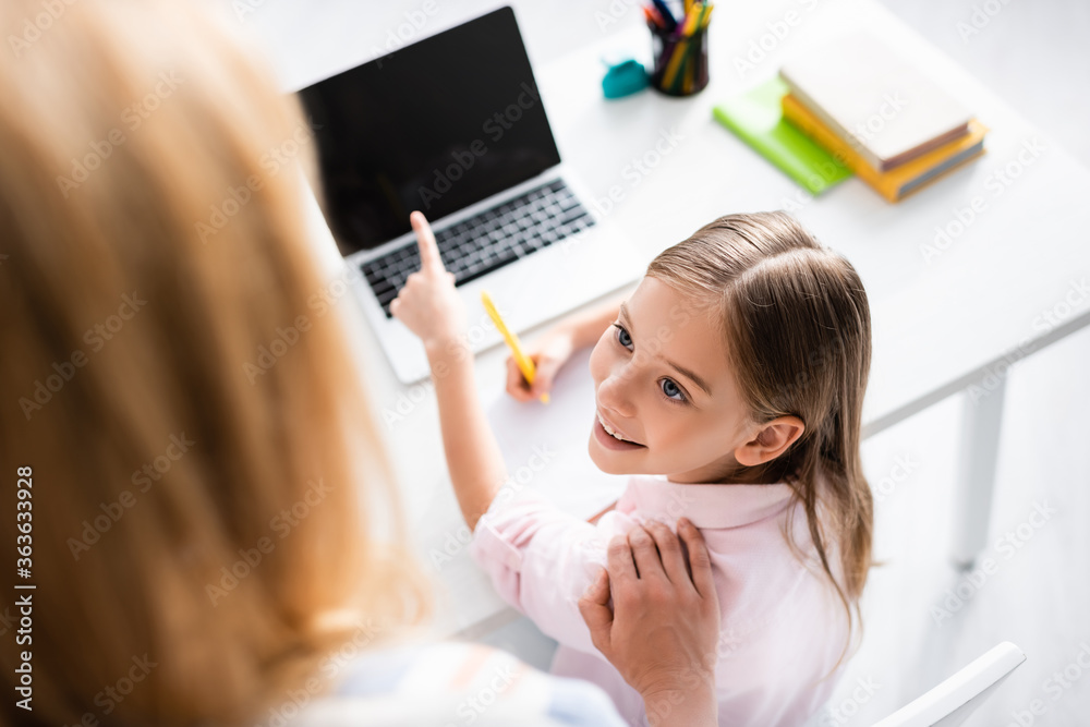 Overhead view of smiling kid pointing with finger at laptop near mother Overhead view of smiling kid pointing with finger at laptop near mother