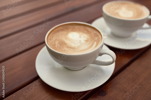 Two cups of cappuccino on the wooden background. Beautiful brown foam, white ceramic cups, place for text