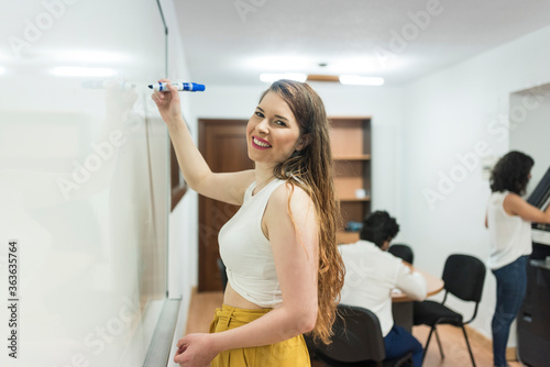 Woman in office writing in board  workers in background