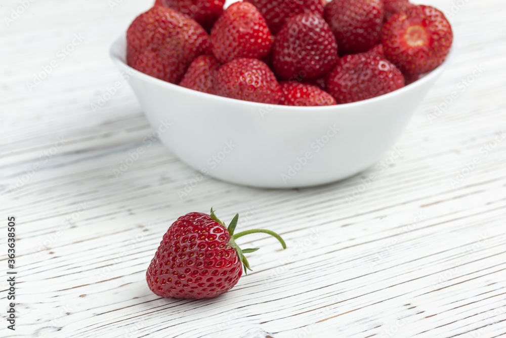 one white plate with strawberries on a wooden background, next to lie one strawberry one white plate with strawberries on a wooden background, next to lie one strawberry