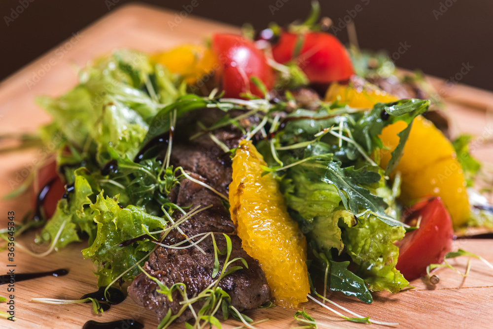 Salad of lettuce, greens, orange, tomato, veal, fresh vegetables, onions, olives on a wooden tray, board, dish. Horizontal photo 