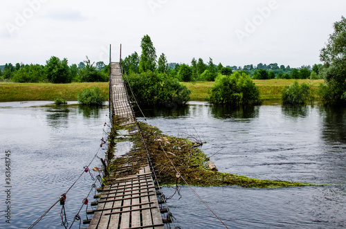 Fotografía Suspension bridge over the river is broken and flooded against the backdrop of a