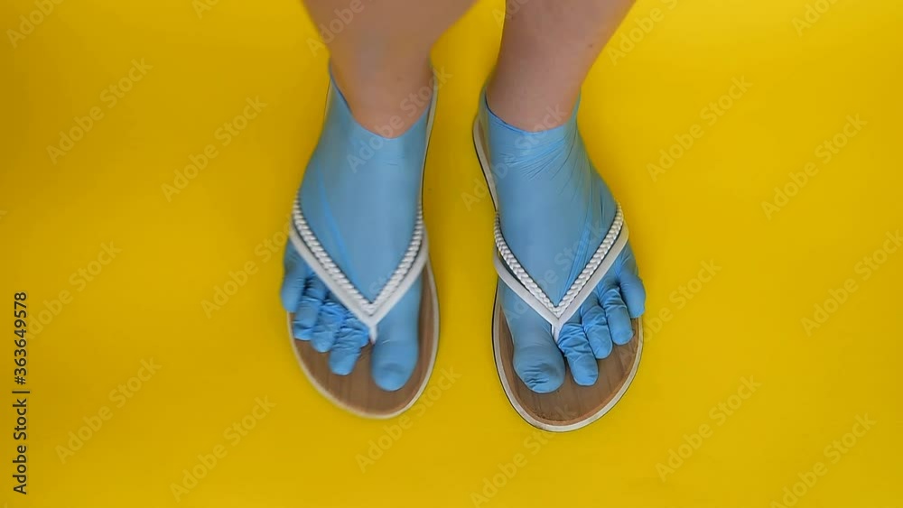 Female legs are dressed in rubber blue medical gloves, shod in white flip flops. Dancing on a yellow uniform background. Comic safe from viruses and diseases summer holiday concept on the beach of the