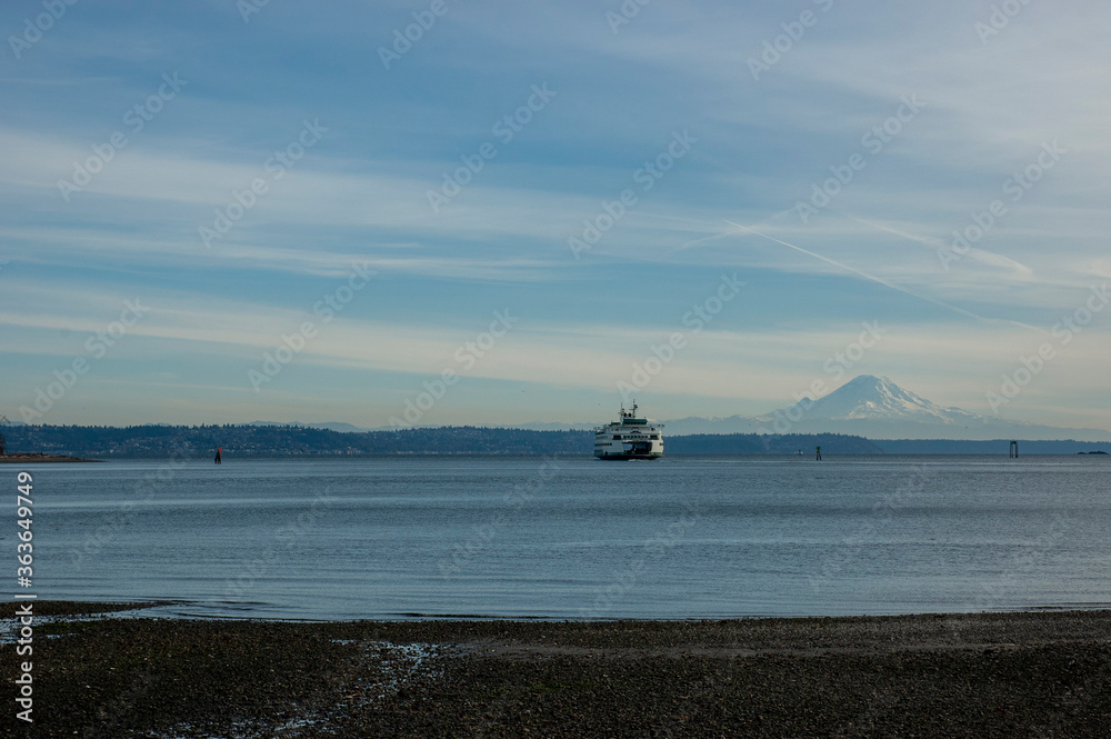 Obraz premium Ferry in Puget Sound against the backdrop of Mount Rainier, with blue sky and some clouds, as seen from Hawley Cove on Bainbridge Island