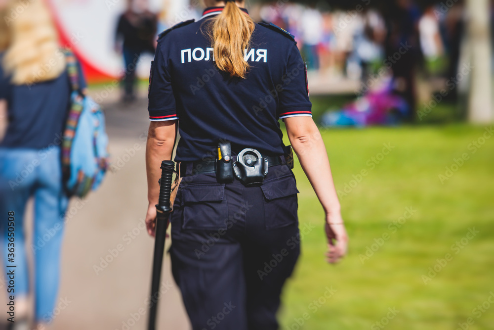 Fototapeta premium Formacja rosyjskiej policji żeńskiej widok z tyłu z emblematem "Policja" na mundurze utrzymuje porządek publiczny po meczu piłki nożnej z tłumem kibiców w tle