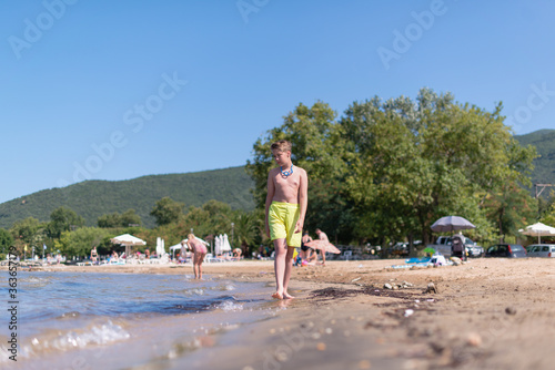 Young blond boy is walking on a beach in yellow swimwear