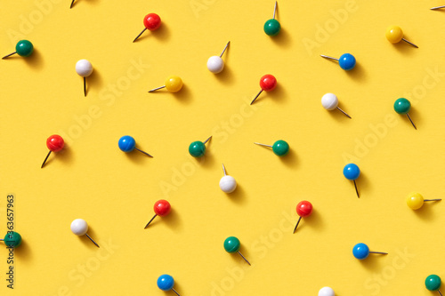 Office supplies pattern of multicolored pins on yellow.
