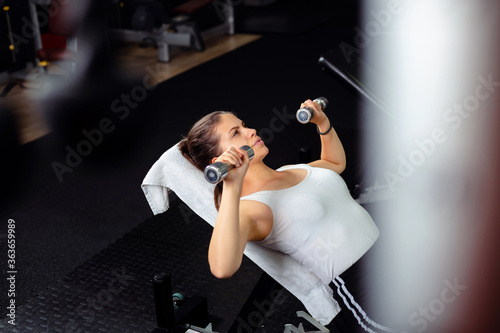 Bilde på lerret Young  and beautiful woman exercise in gym, she is doing incline bench press wit