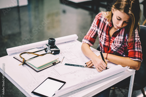 Obraz na plátně Professional female architect drawing blueprint of construction using stationery