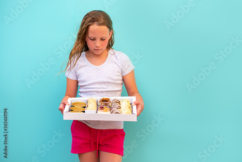 Cute teenage girl freckles woman holding box with dessert chocolate and vanilla mousse decorated with sweet cream  cookies and candy in a glass jar  fruit sushi  alfajores  macaroons and creme brulee.