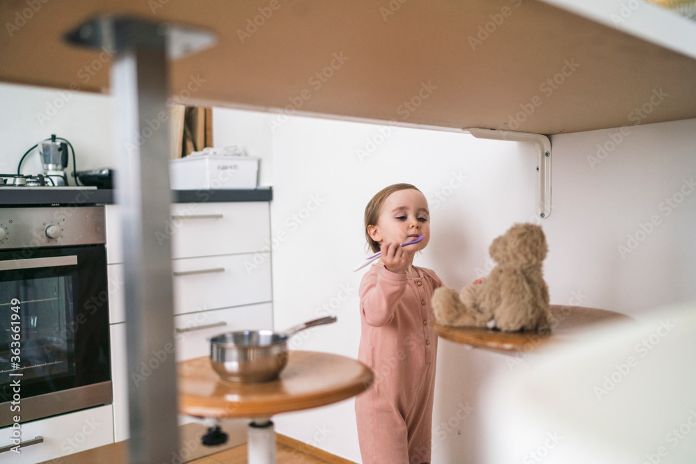 Cute girl feeding teddy bear in kitchen