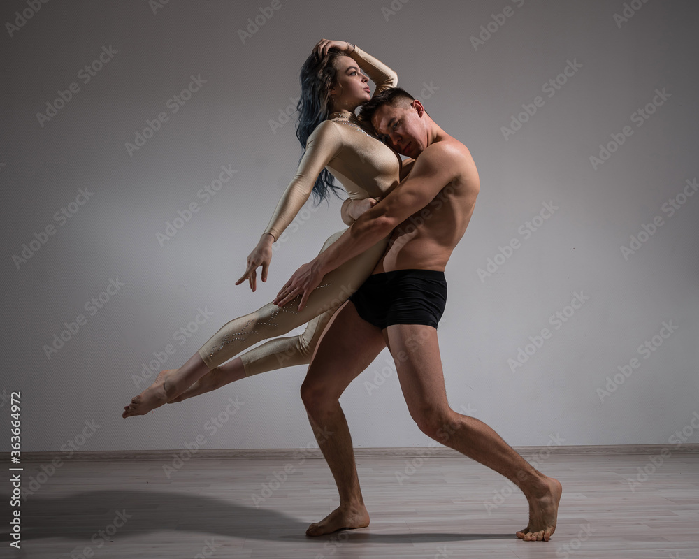 Acrobatic couple perform number on a white background. A duet of gymnasts rehearsing a performance with support. A man and a very flexible woman are dancing. Acrobatic couple perform number on a white background. A duet of gymnasts rehearsing a performance with support. A man and a very flexible woman are dancing.