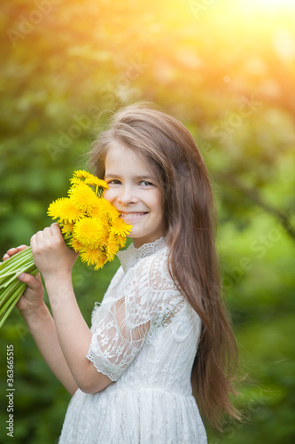 fashionable girl in a light dress poses and holds a large bouquet of yellow dandelions