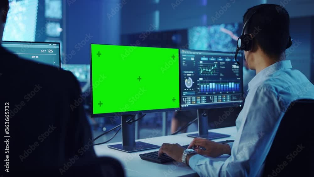 Confident Male Data Scientist Works on Personal Computer with Green Screen Template Wearing a Headset in Big Control and Monitoring Room. Young Engineer in a Call Center Office Room with Colleagues. Confident Male Data Scientist Works on Personal Computer with Green Screen Template Wearing a Headset in Big Control and Monitoring Room. Young Engineer in a Call Center Office Room with Colleagues.
