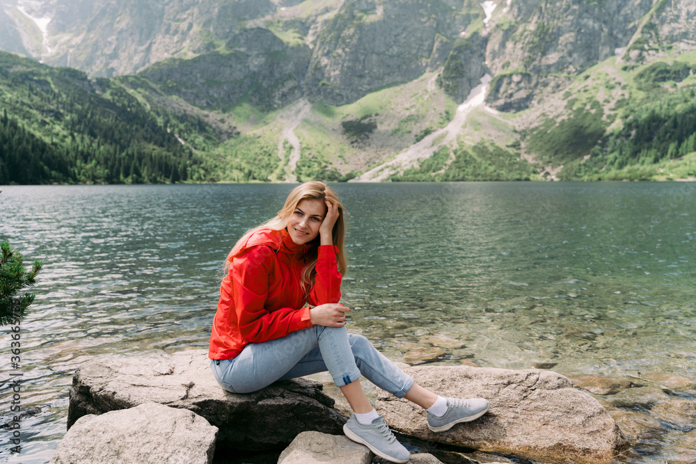 Happy woman sitting on large stone near lake water.